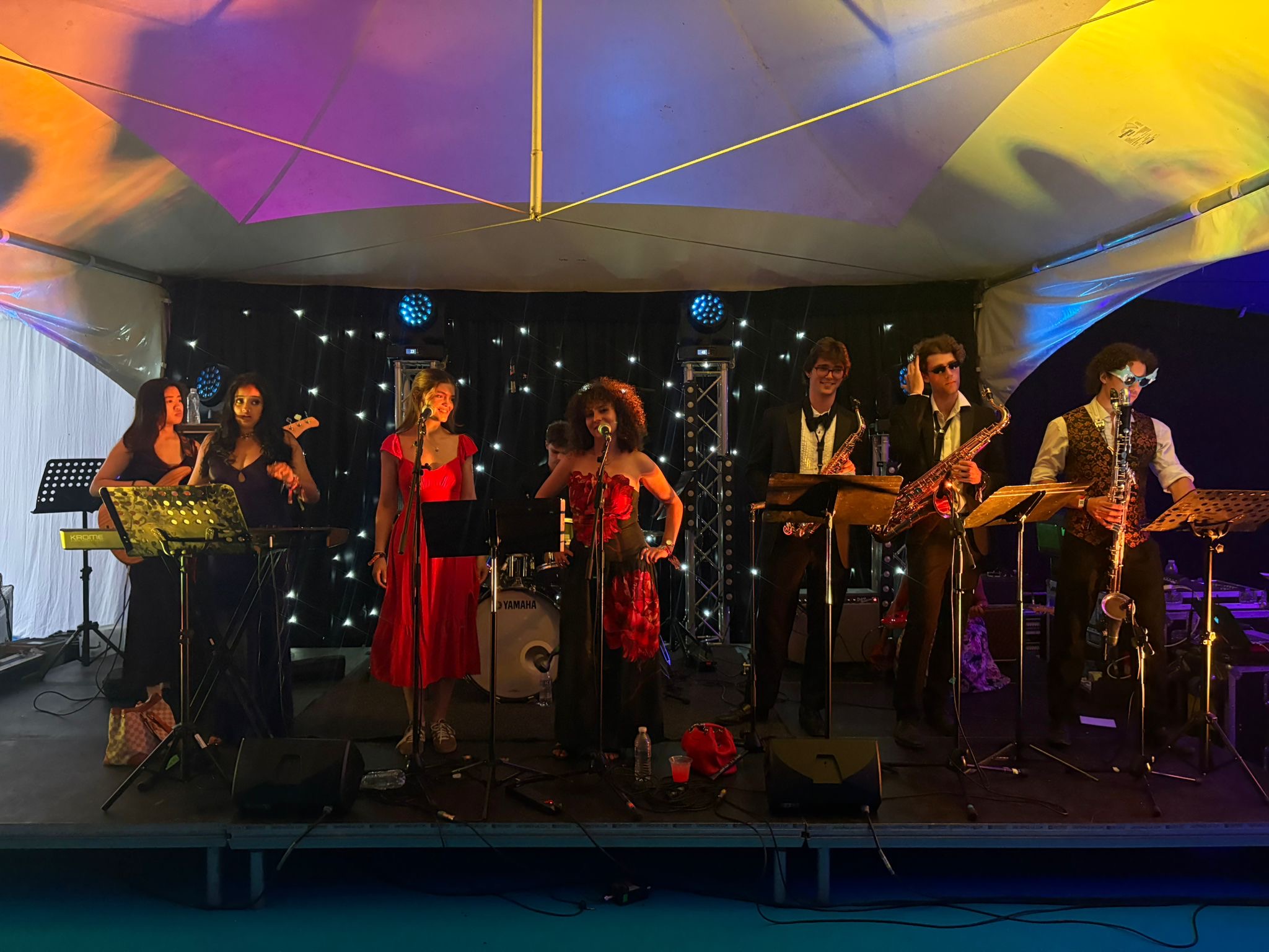 The band on stage under a marquee with coloured lights