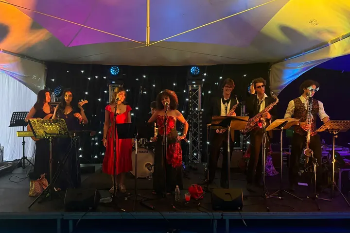 The whole band on a marquee stage under coloured lights